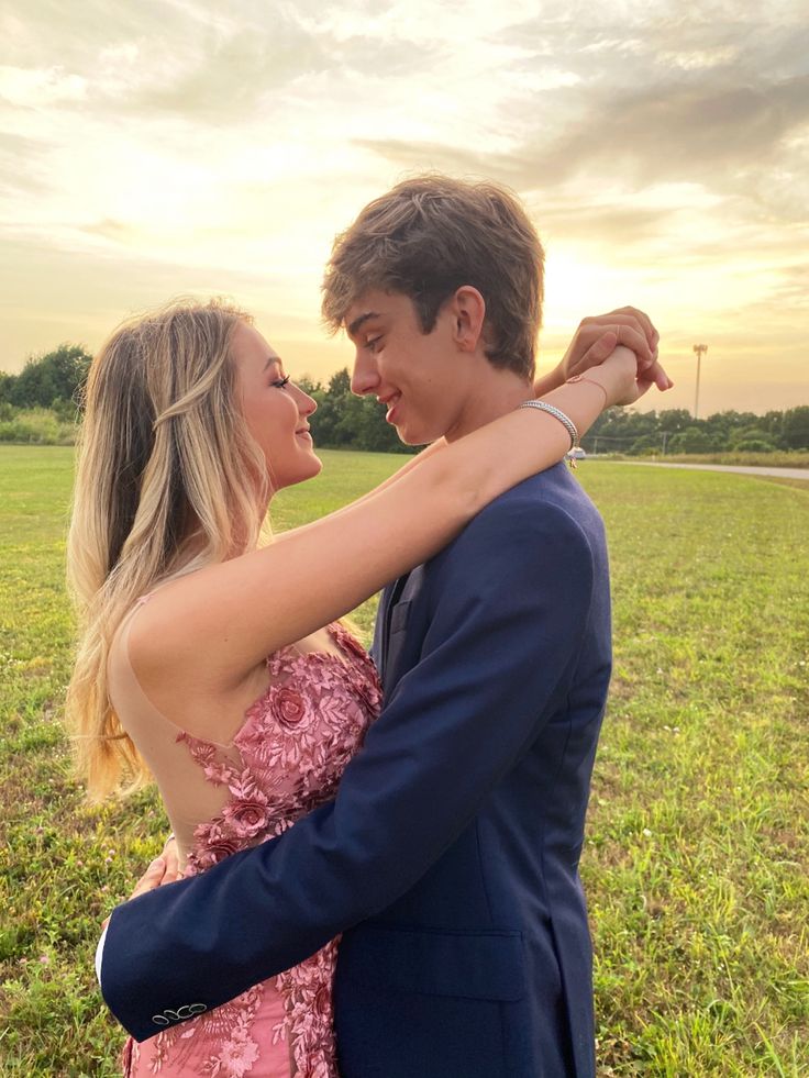 a young man and woman embracing each other in the middle of a field at sunset