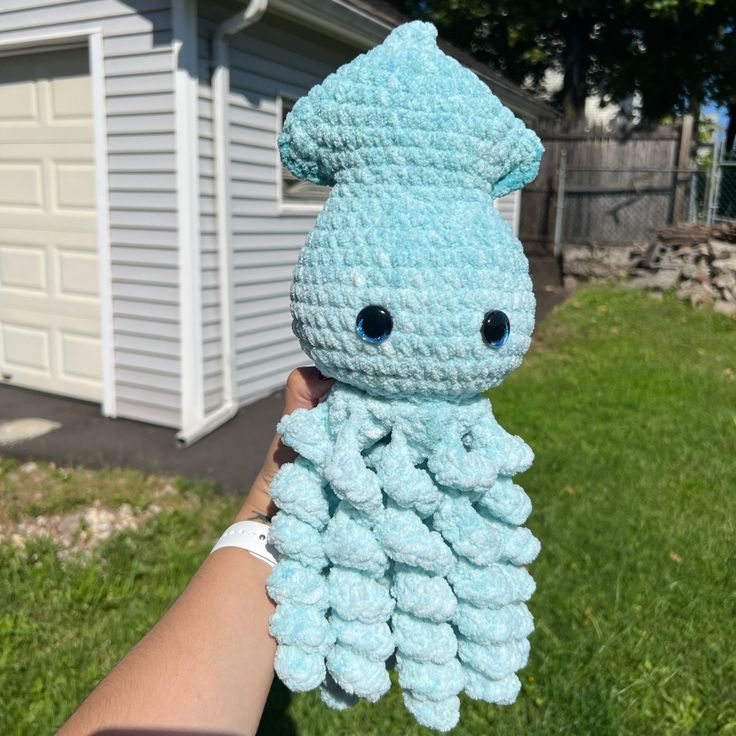 someone holding up a crocheted stuffed animal in front of a house and yard