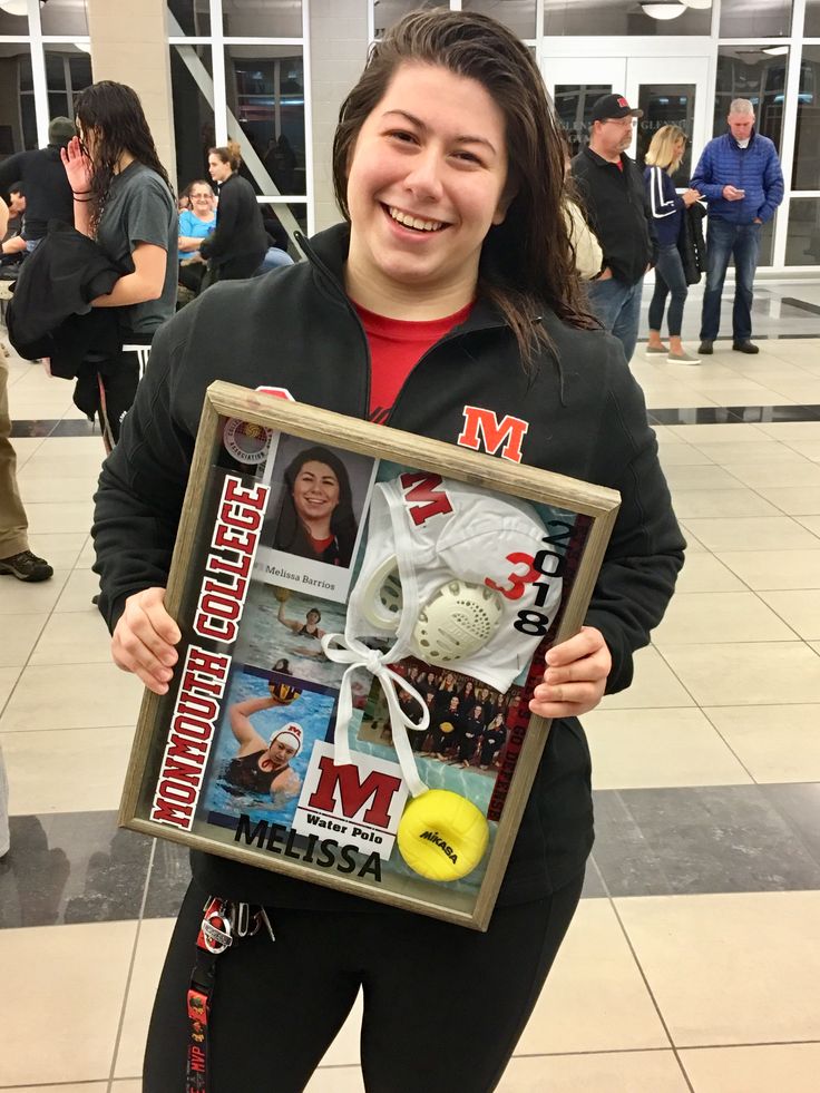 a woman holding up a framed photo with sports memorabilia in front of her and smiling at the camera