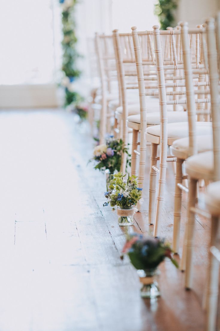 rows of wooden chairs lined up with flower arrangements on the back and side of them