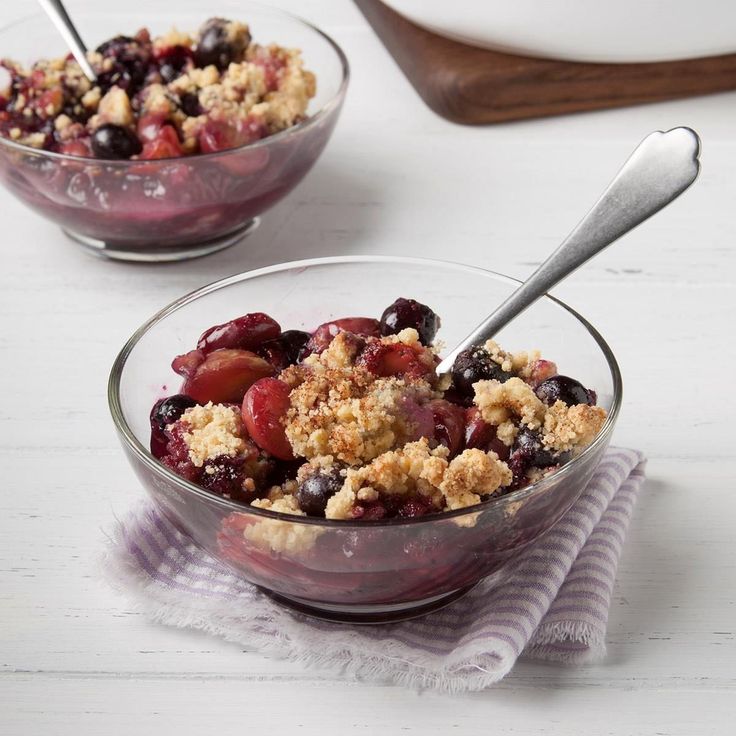 two bowls filled with fruit and crumbs on top of a white table next to a cutting board