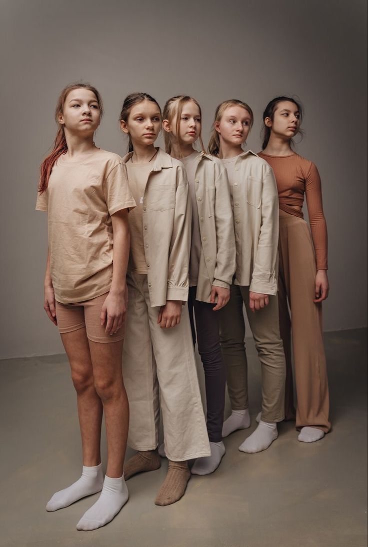 five models standing in front of a gray background, all wearing beige clothing and white shoes