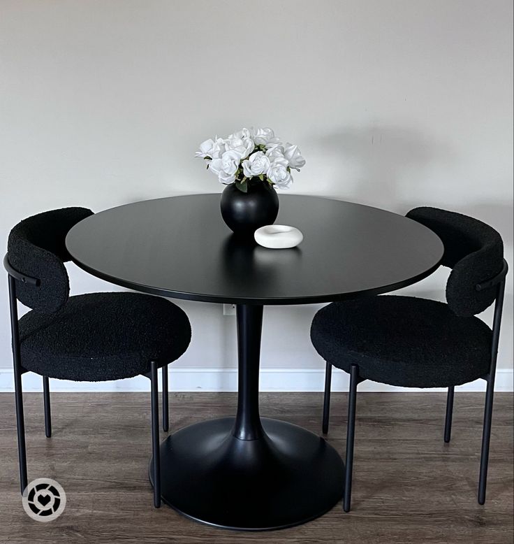 a black table with four chairs around it and a vase filled with flowers on top