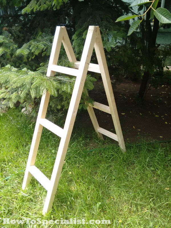 a wooden ladder sitting on top of a lush green field next to a tree and bushes