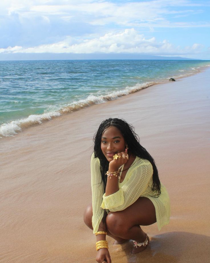 a woman kneeling down on the beach next to the ocean