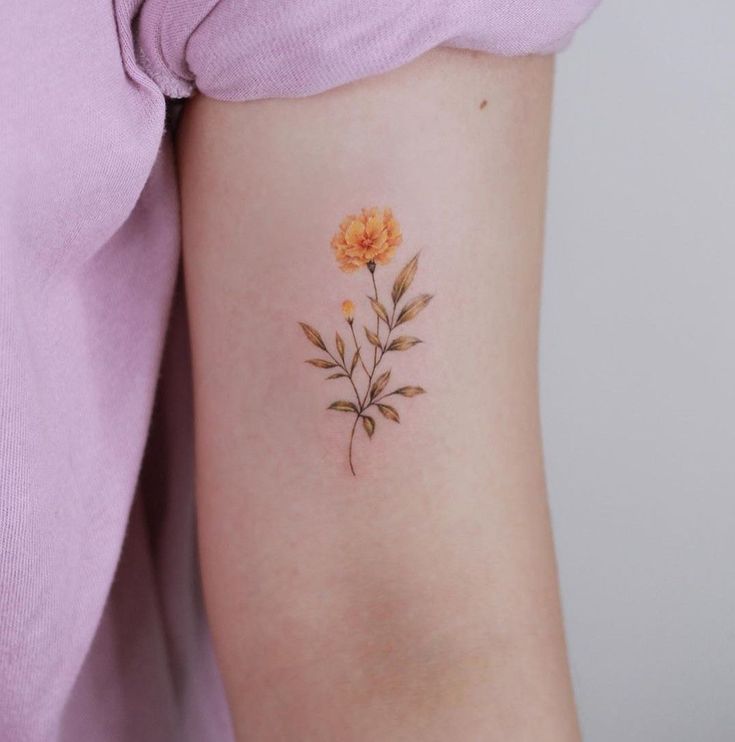 a woman's arm with an orange flower tattoo on the left side of her arm