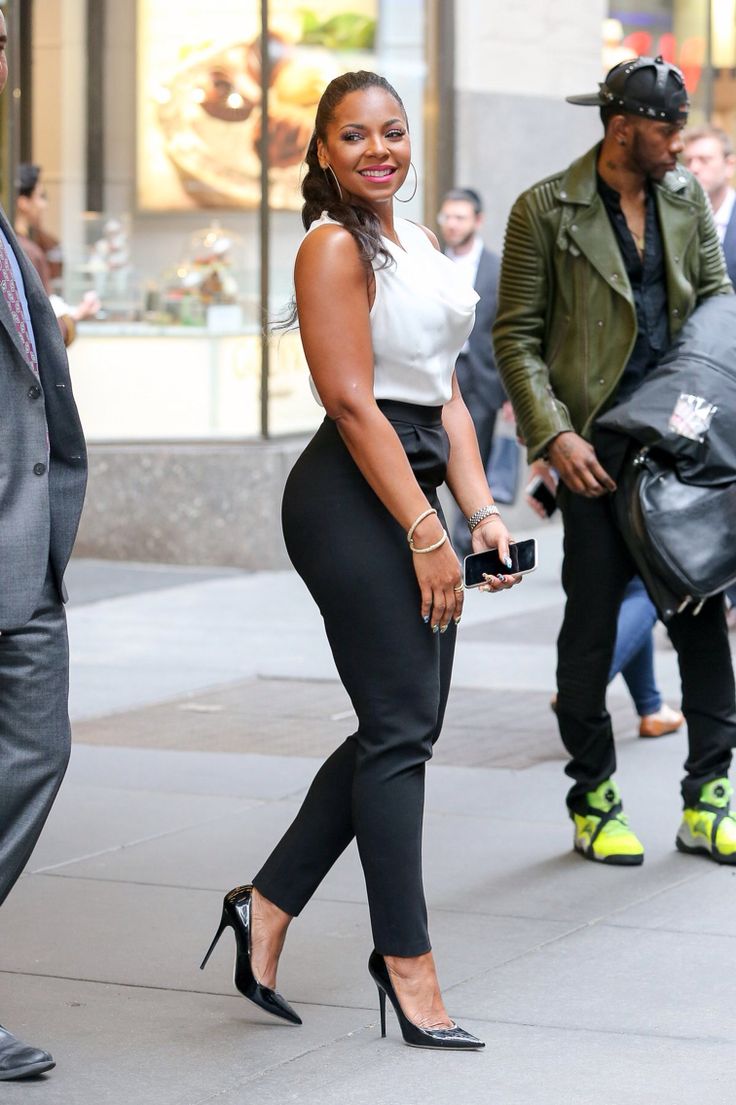 a woman in tight black pants and heels walking down the street with a man behind her