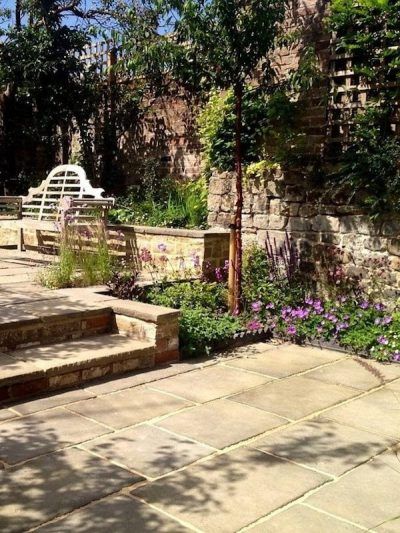 an outdoor patio with stone steps and flowers in the foreground, surrounded by greenery