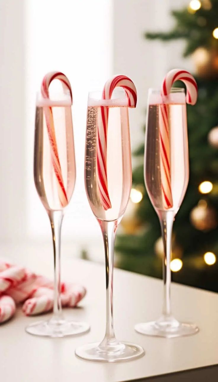 three wine glasses with candy canes in them on a table next to a christmas tree