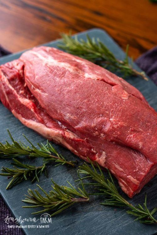 a piece of meat sitting on top of a cutting board next to some green herbs