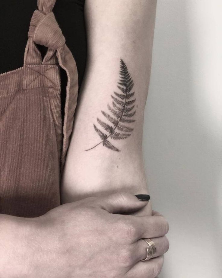 a woman's arm with a fern tattoo on the left side of her arm