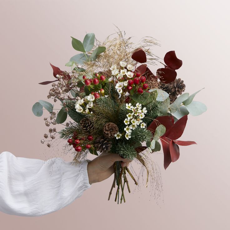 a person holding a bouquet of flowers and greenery on a pink background in the image