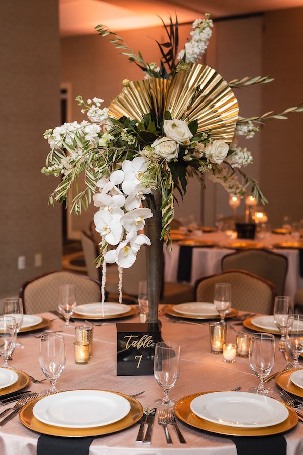 a tall vase filled with white flowers and greenery on top of a dining table