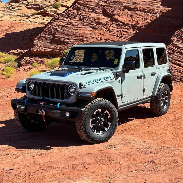 a white jeep parked on top of a red dirt field next to a rock formation