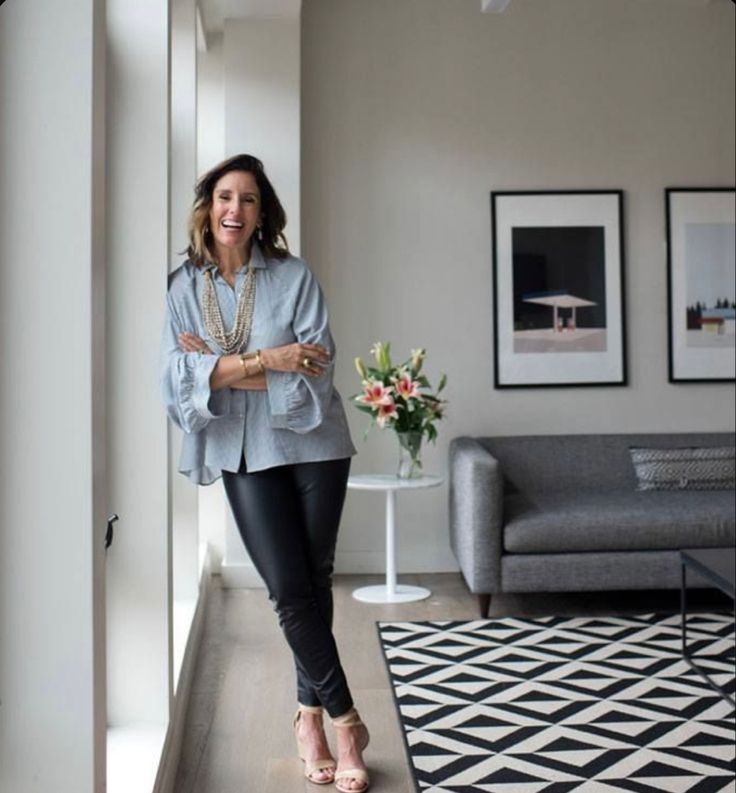 a woman standing in a living room next to a gray couch and black and white rug