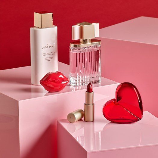 two bottles of perfume and a heart shaped box on a pink surface with red background