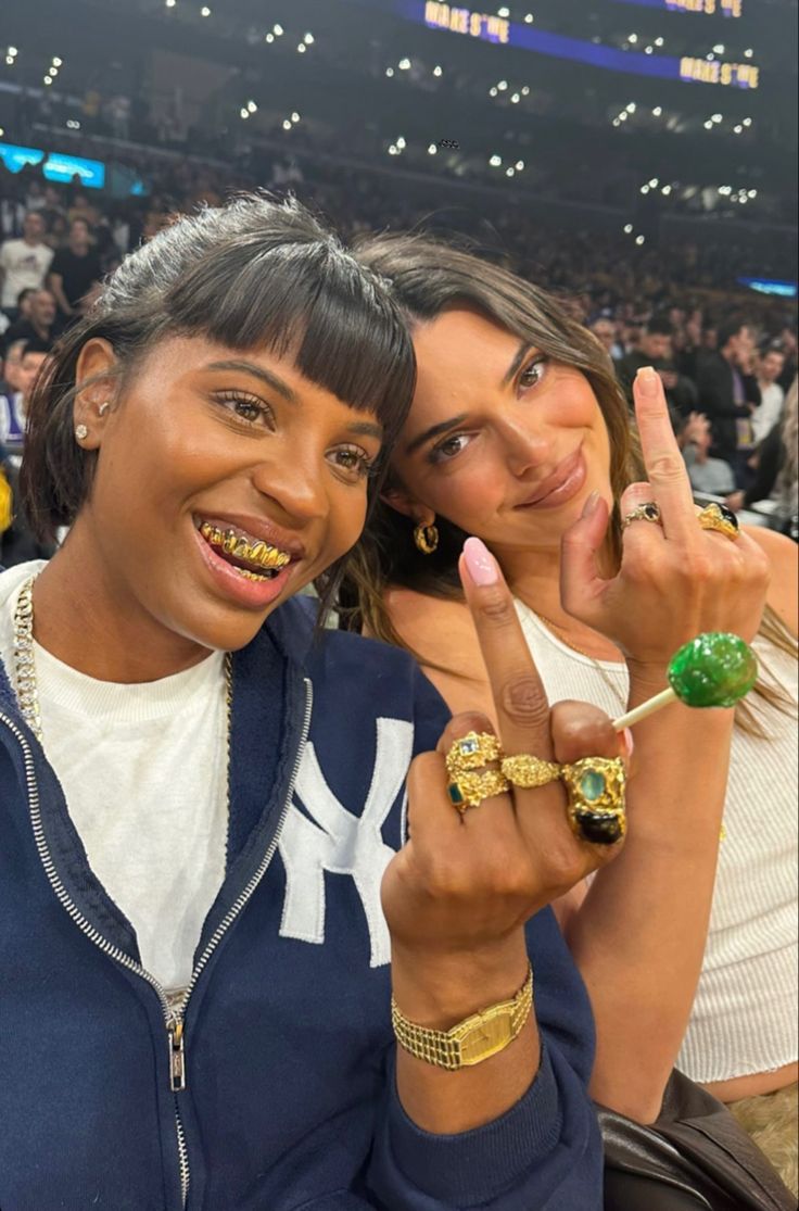 two women posing for the camera with their fingers in the air at a sporting event