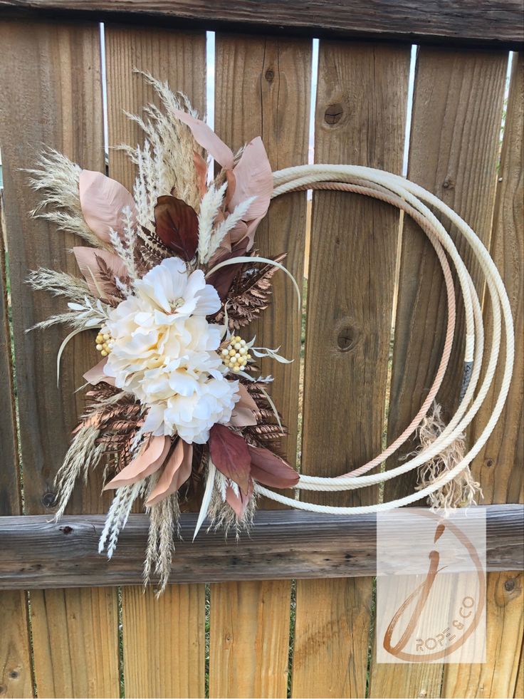 a wreath with flowers and feathers hanging on a fence