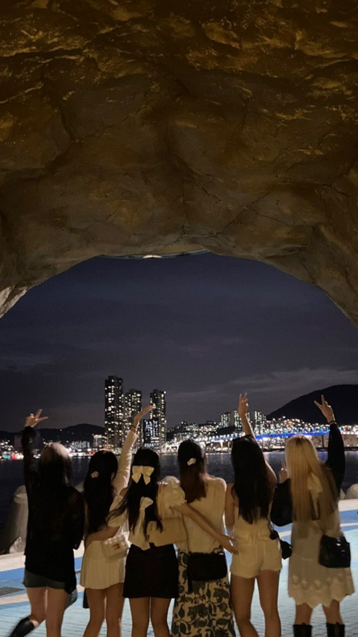 group of young women standing together in front of a rock formation with city lights behind them