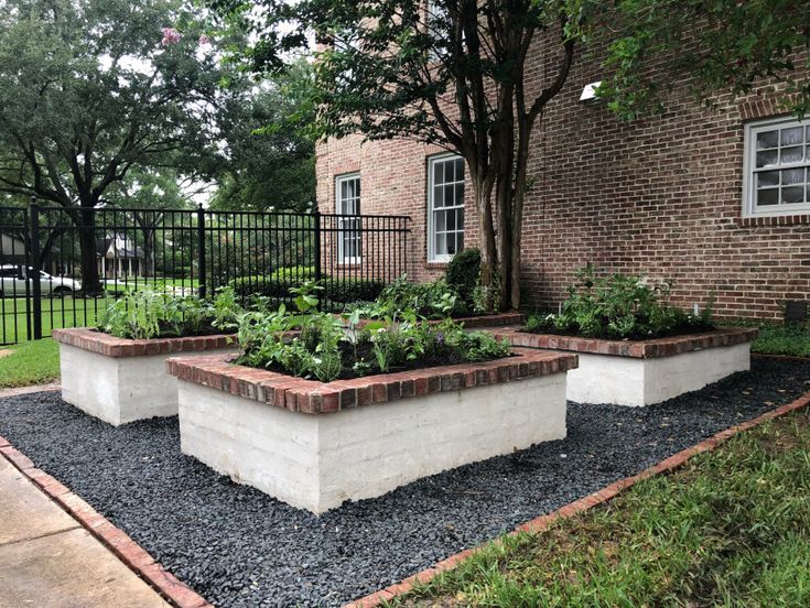 an outdoor garden area with raised planters and brick edgings in front of a brick building