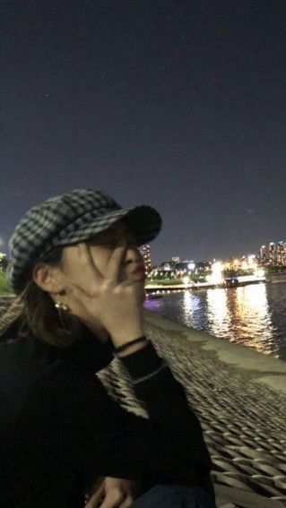 a woman sitting on the beach at night with her hand to her face, looking into the distance