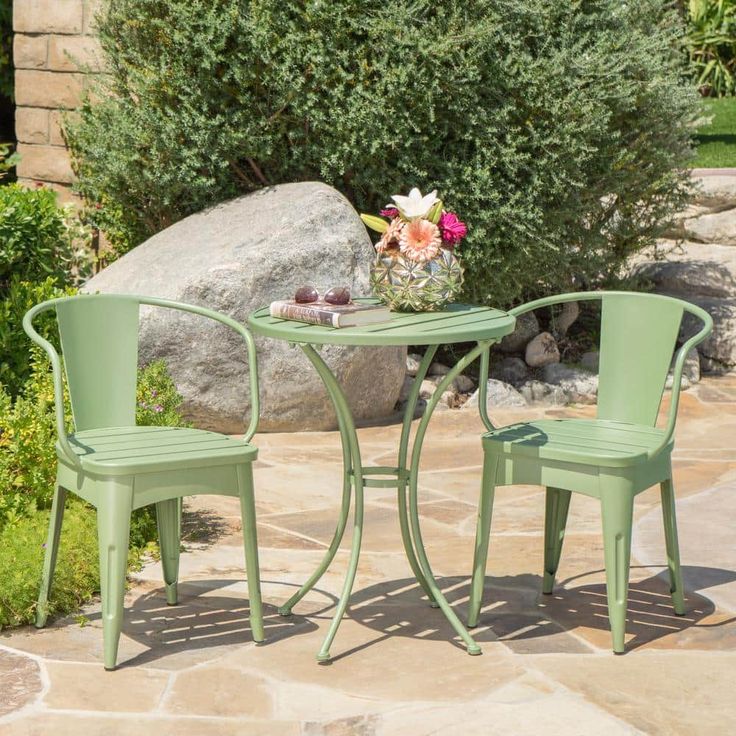 two green chairs and a small table on a stone patio