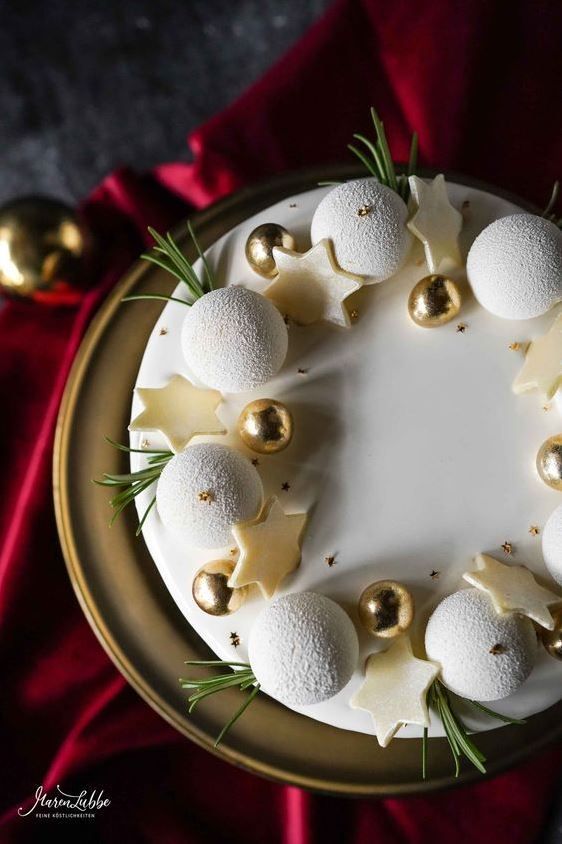 a cake with white frosting and gold ornaments on top, surrounded by greenery