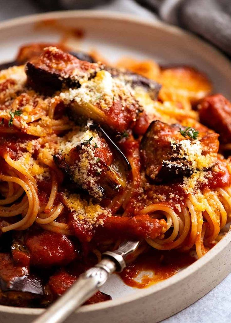 a bowl filled with pasta and meat covered in marinara sauce next to a fork