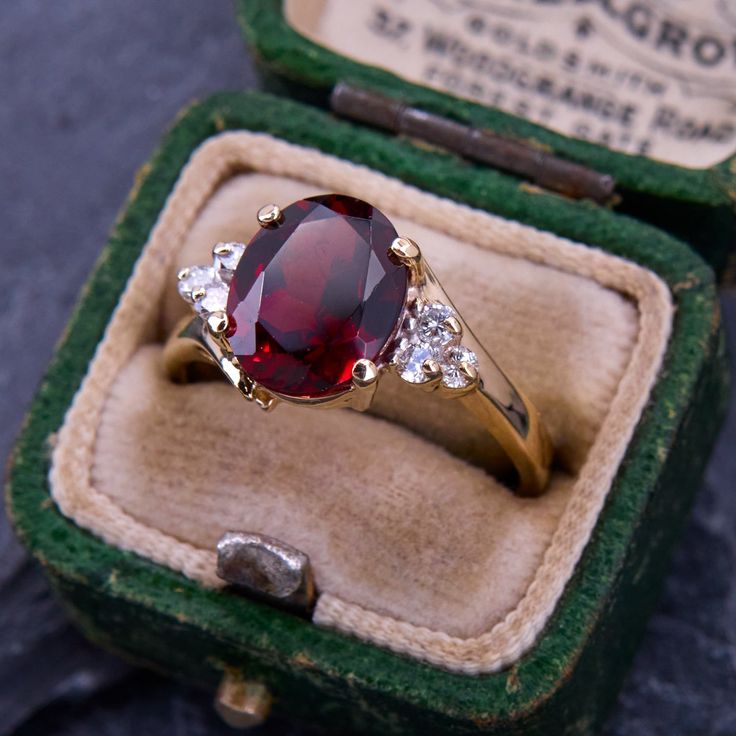 a ring with a large red stone surrounded by three small white stones in a green velvet box