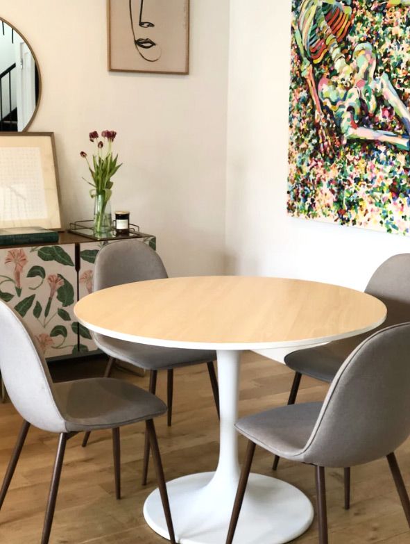 a dining room table with four chairs and a round mirror on the wall above it