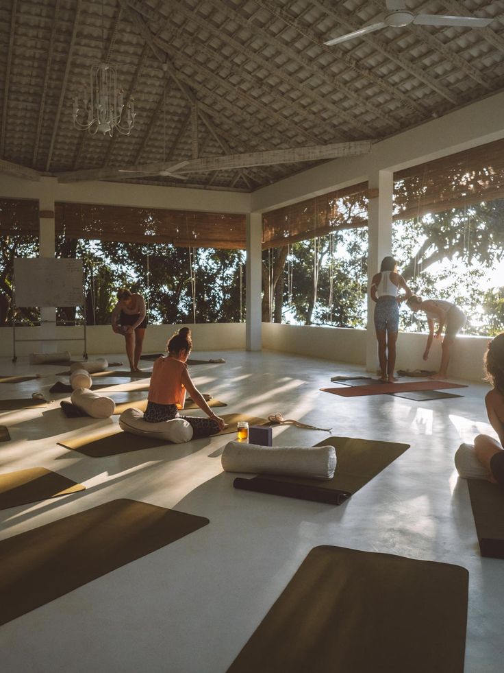 a group of people sitting on yoga mats in a room with large windows and sun shining through them