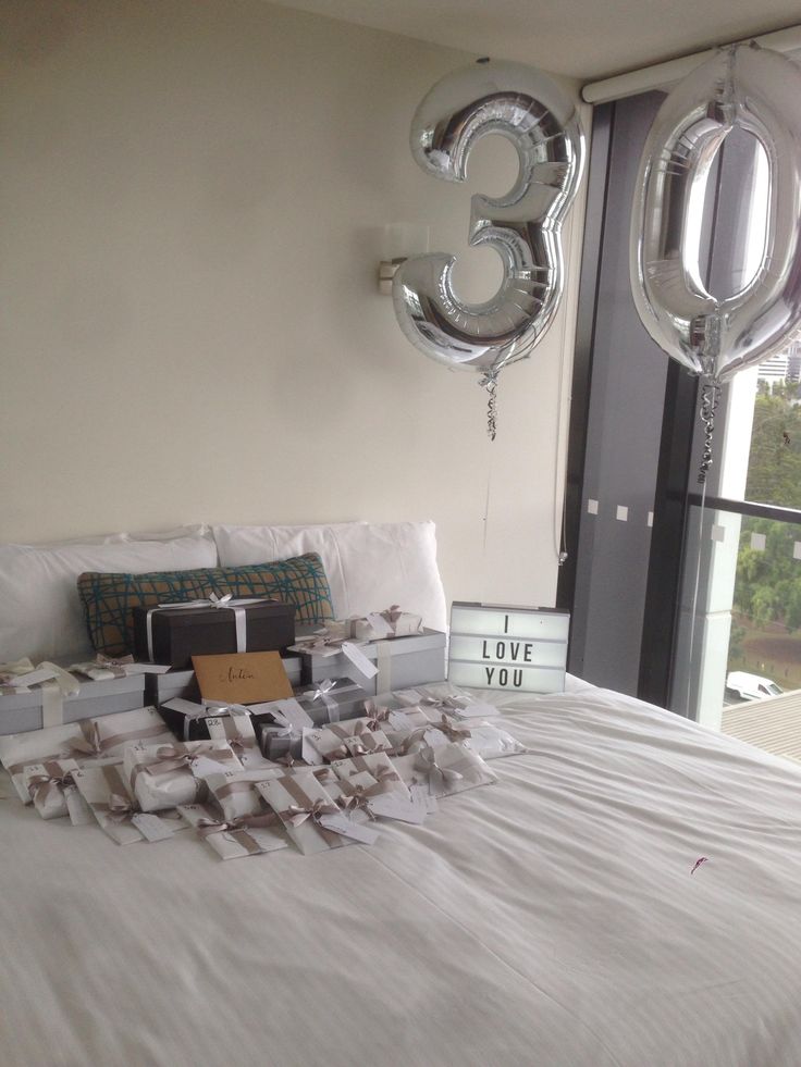 a bed with balloons and gifts on top of it in front of a large window