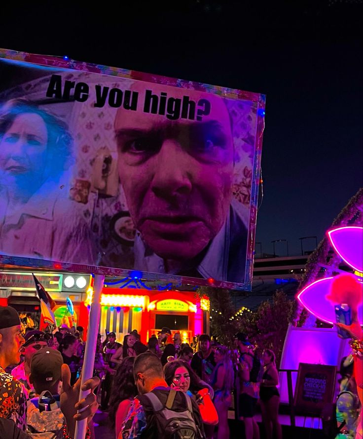 a crowd of people standing around in front of a large billboard with the words are you high?