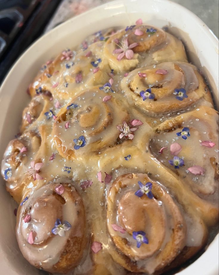 a white bowl filled with cinnamon rolls covered in icing