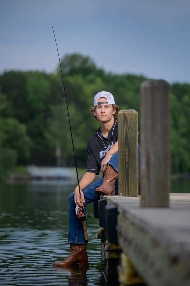 a young man sitting on a dock holding a fishing pole