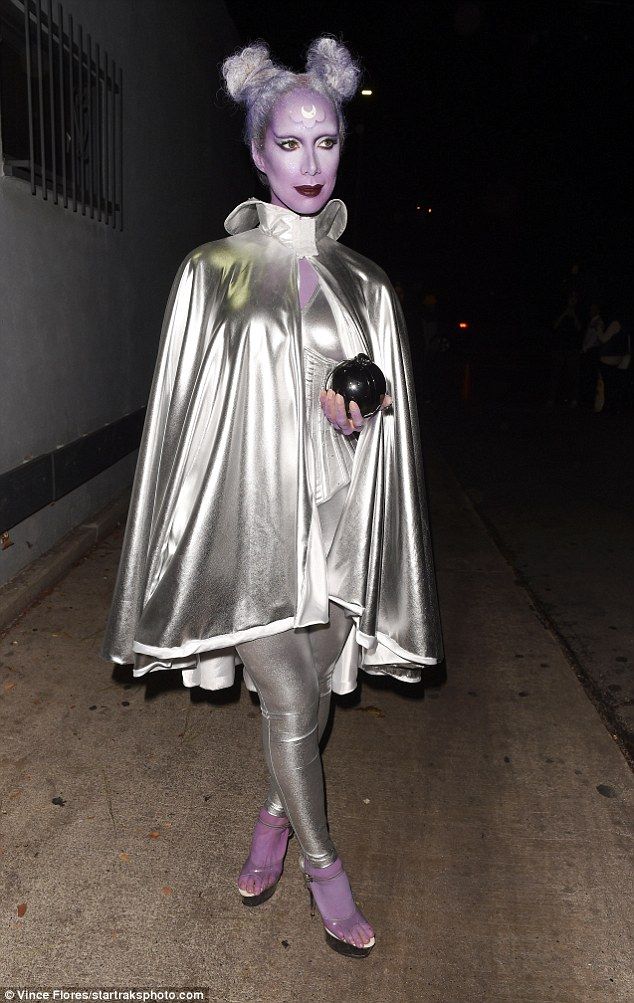 a woman dressed in silver is walking down the street with purple hair and makeup on