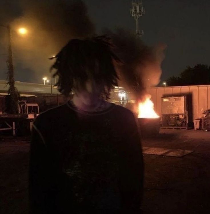 a man with dreadlocks standing in front of a fire