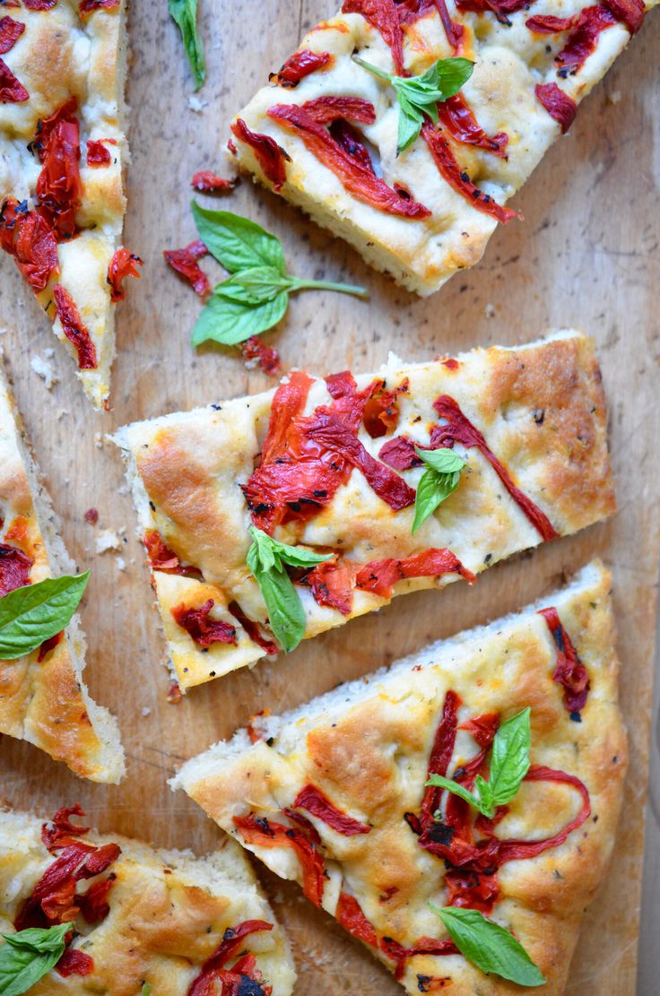 several slices of pizza on a cutting board with basil leaves and red peppers scattered around them