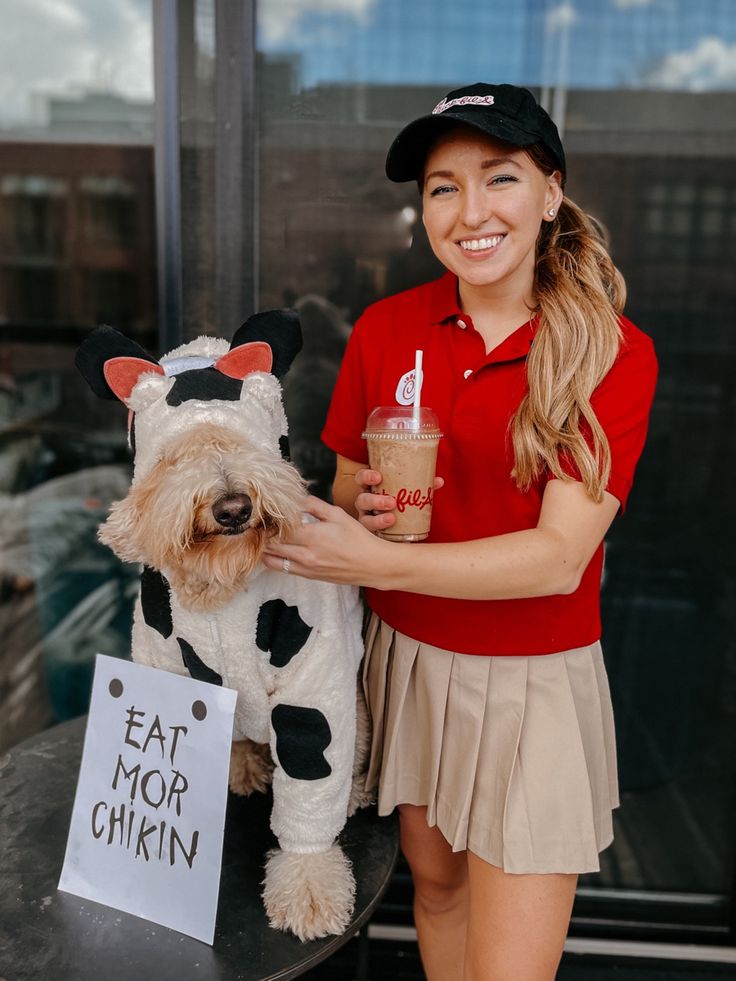 a woman in a red shirt is petting a small dog wearing a cow costume