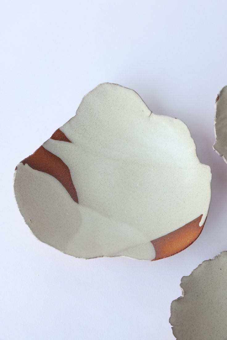 two pieces of white and brown pottery sitting next to each other on a white surface