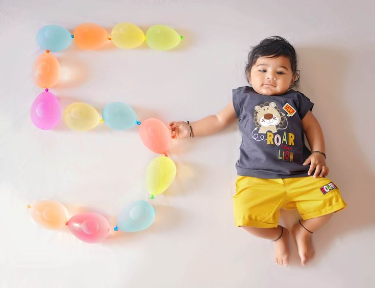 a little boy laying on the floor with balloons in front of him that spell out the letter e