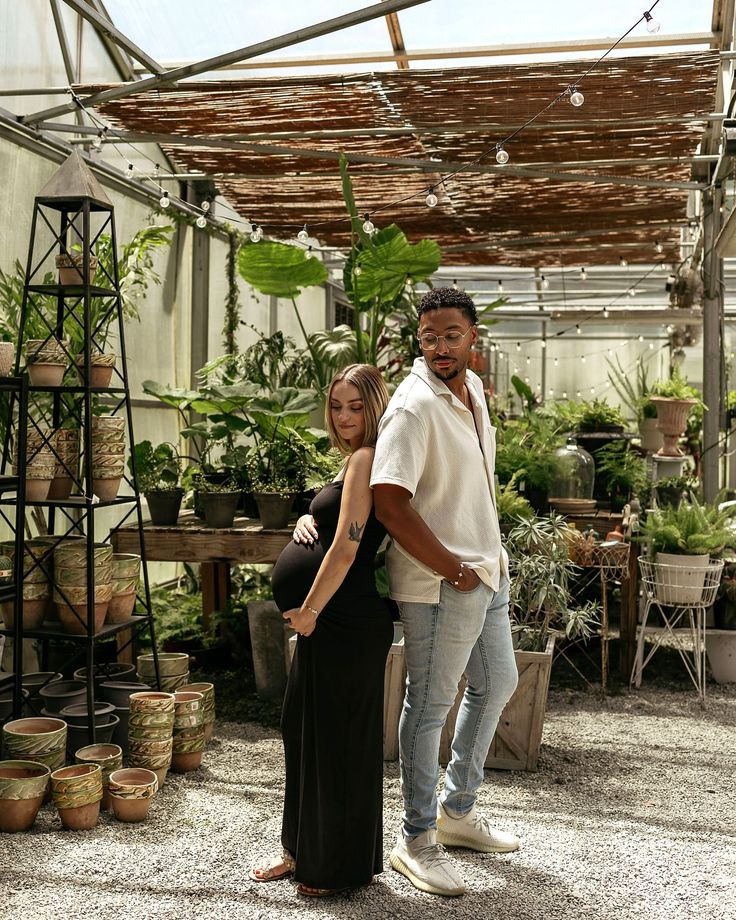 a man and woman standing next to each other in a greenhouse with potted plants