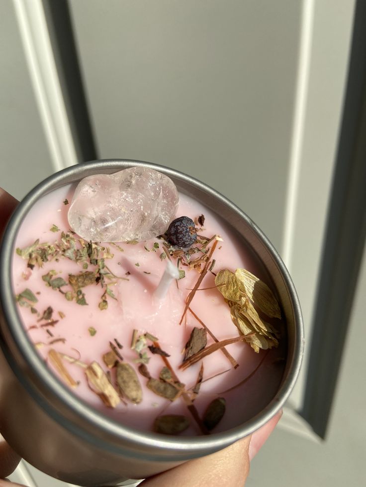 a person holding a cup filled with pink liquid and various small things on top of it