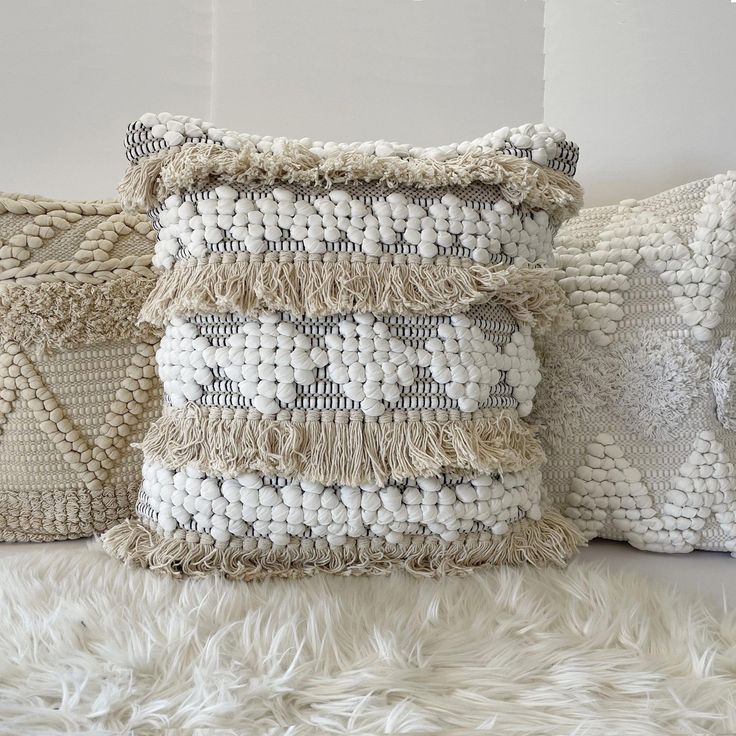 three decorative pillows sitting on top of a white furnishing covered floor next to a wall