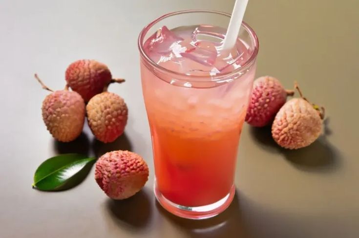 a glass filled with pink liquid next to some fruit on a table and one has a straw in it