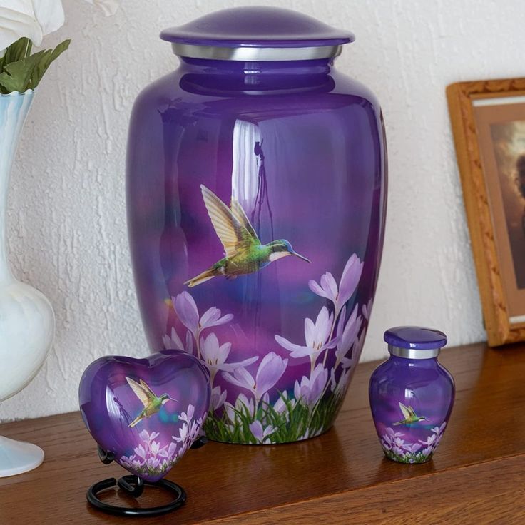 a purple vase sitting on top of a wooden table next to two small jars and a flower pot