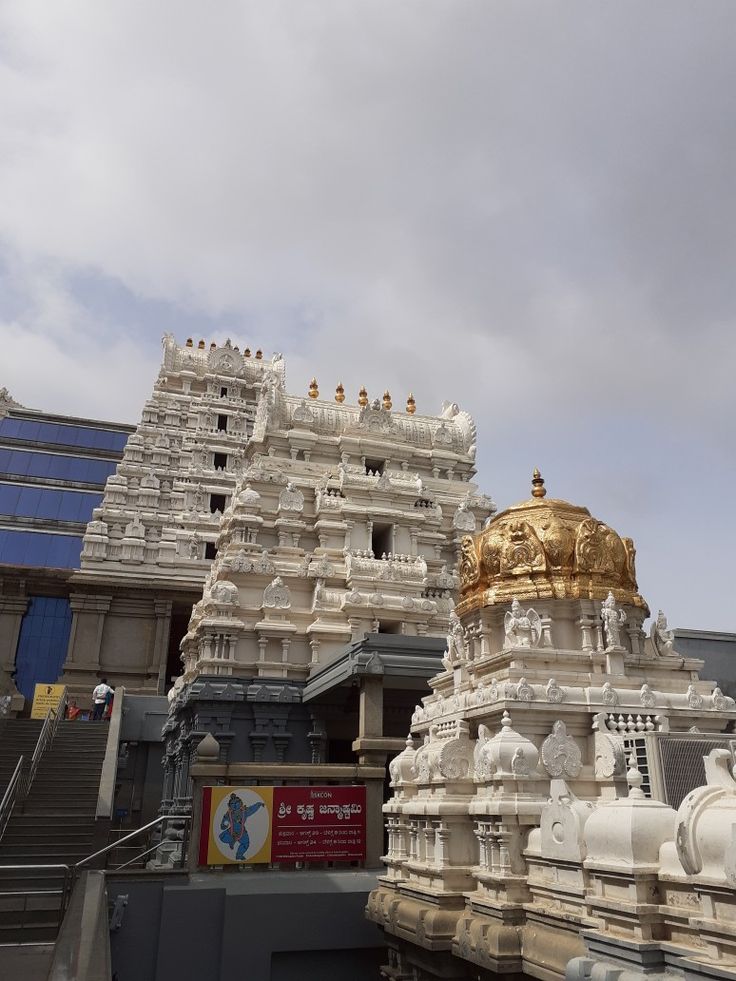 an ornate white and gold building with stairs leading up to the top, in front of a cloudy sky