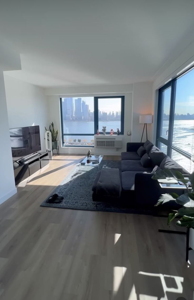 a living room with hardwood floors and large windows overlooking the water in front of it