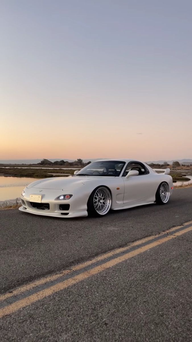 a white sports car is parked on the side of the road next to some water