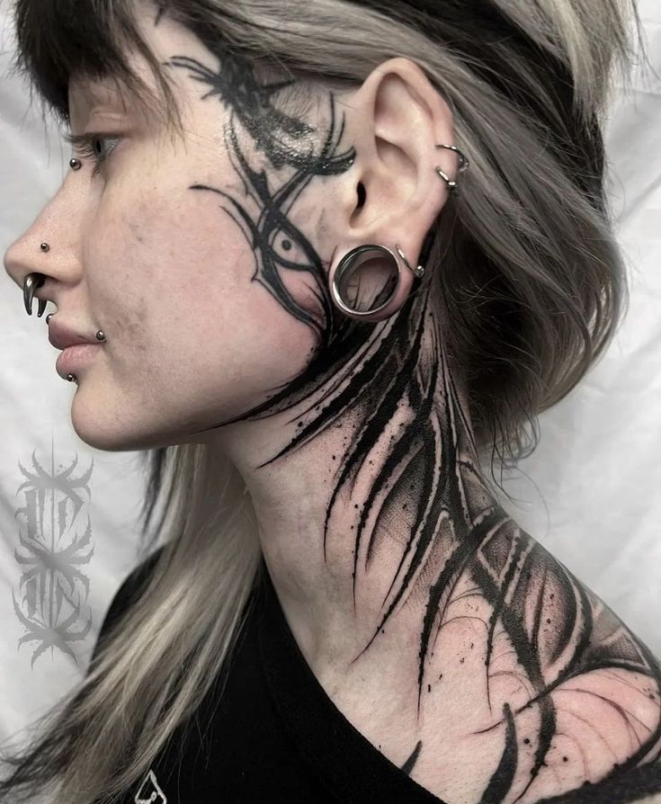 a woman with black ink on her face and behind her ear is a tattoo design